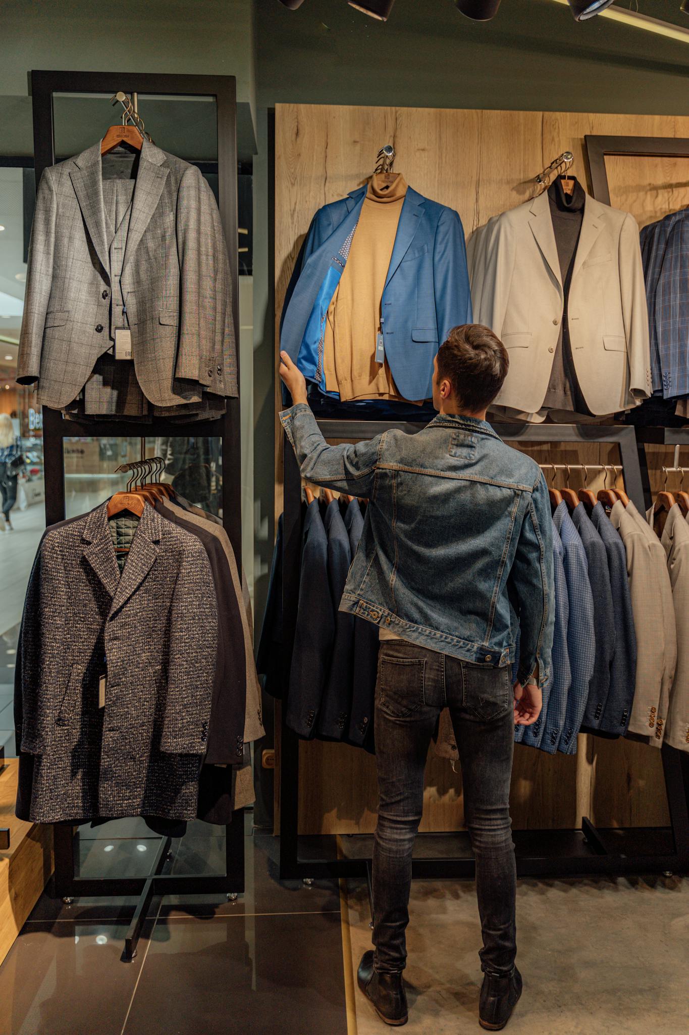 A man examines suits in a stylish fashion store display, highlighting modern shopping choices.