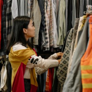 A young woman browsing clothes in a vintage store with colorful outfits.