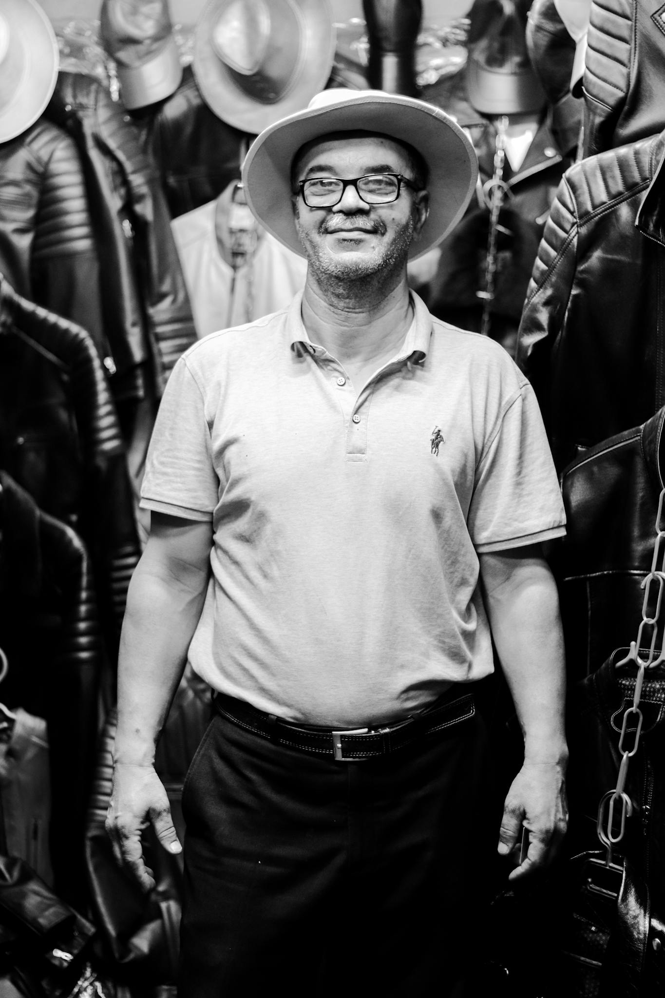 Smiling man wearing a hat, surrounded by leather jackets and hats in a store.