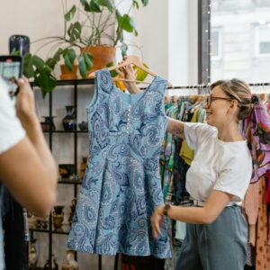 Woman happily showcasing a blue dress during a boutique sale, enhancing live shopping experience.